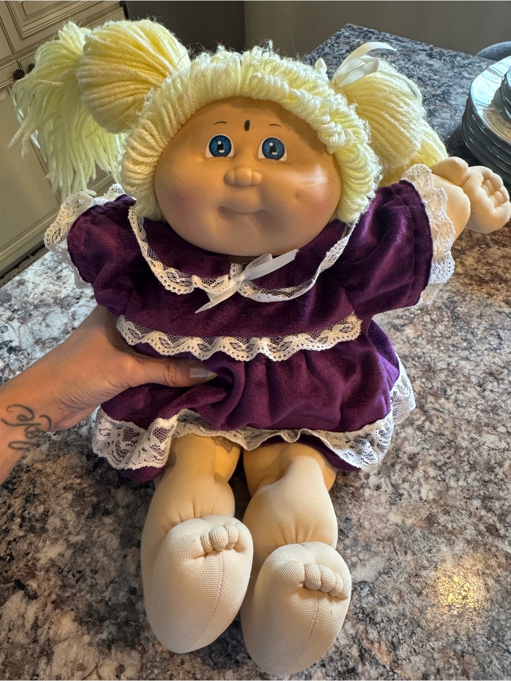 A Cabbage Patch Kid doll with blonde yarn hair and a purple dress
